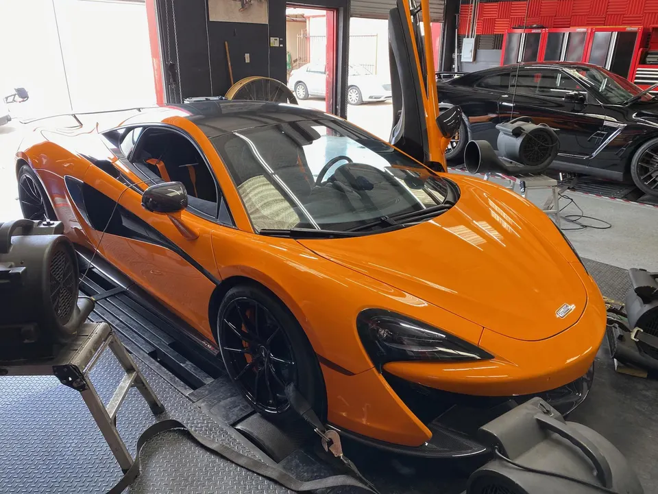 Orange McLaren supercar on a dyno at a performance tuning shop with a black Nissan GT-R in the background.