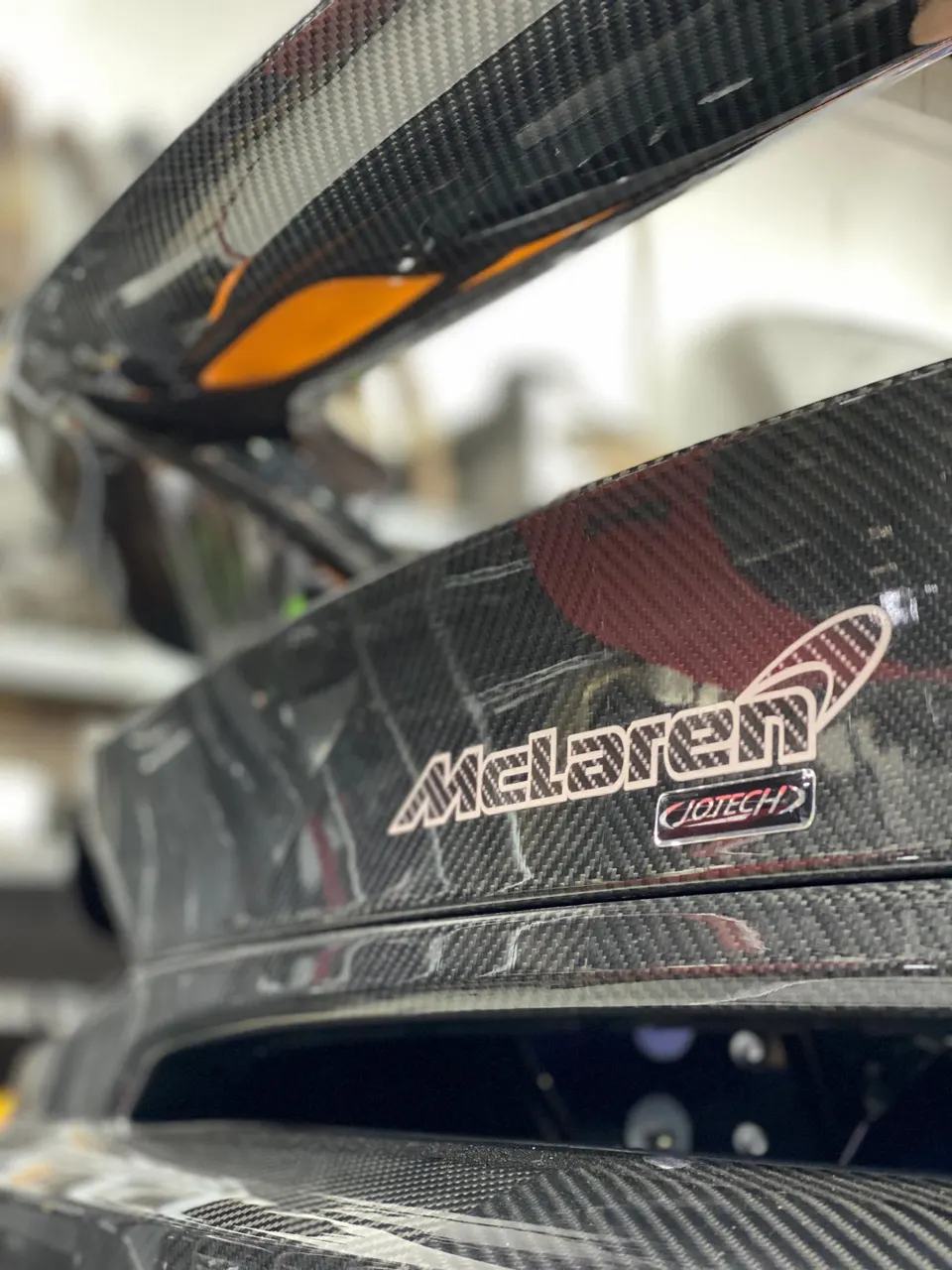 Close-up of a McLaren's carbon fiber rear wing with a Jotech decal, showcasing the intricate weave.