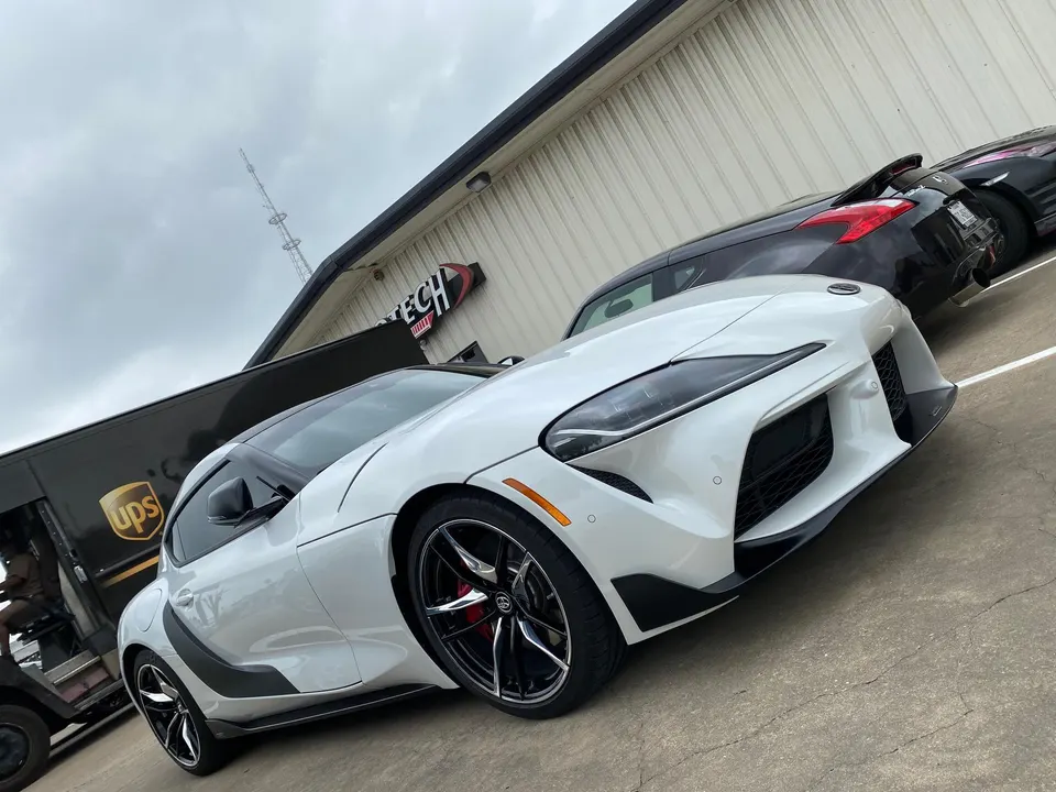 White Toyota Supra parked outside Jotech Motorsports performance shop with aftermarket wheels.