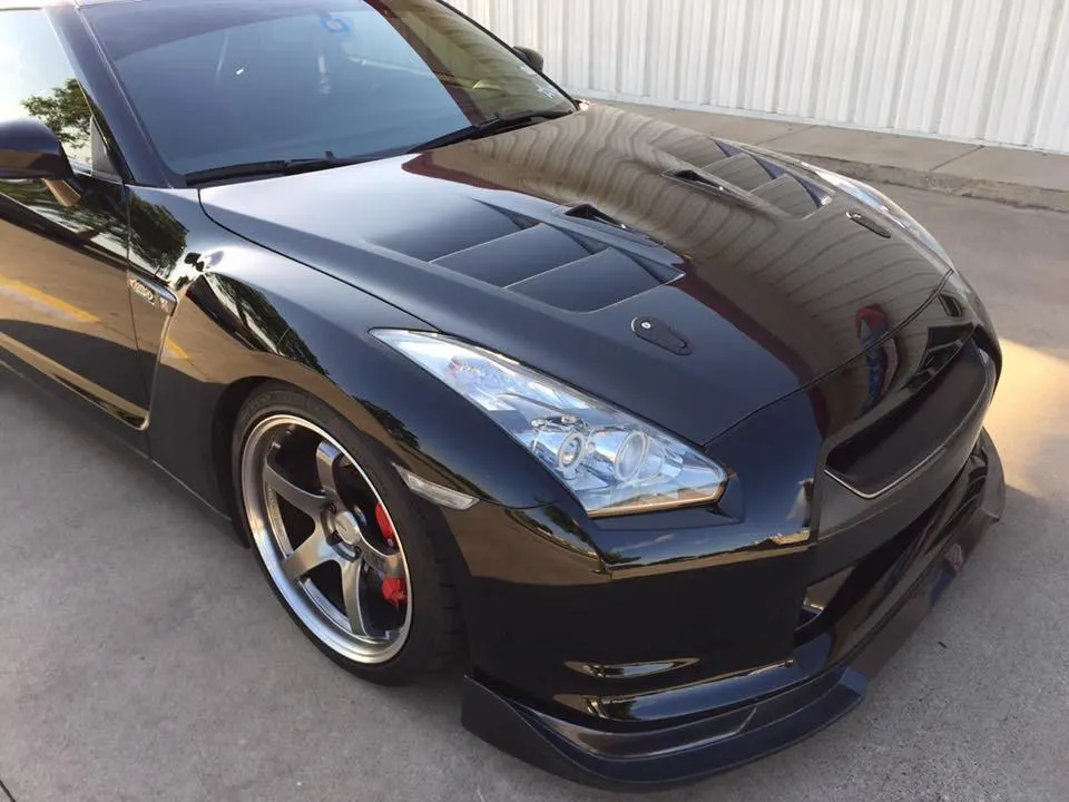 Black Nissan GT-R with aftermarket vented hood, front splitter, and custom bronze wheels with red brake calipers.