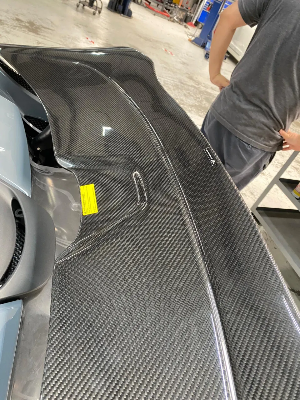 Close-up of a carbon fiber engine cover on a McLaren in a workshop setting.