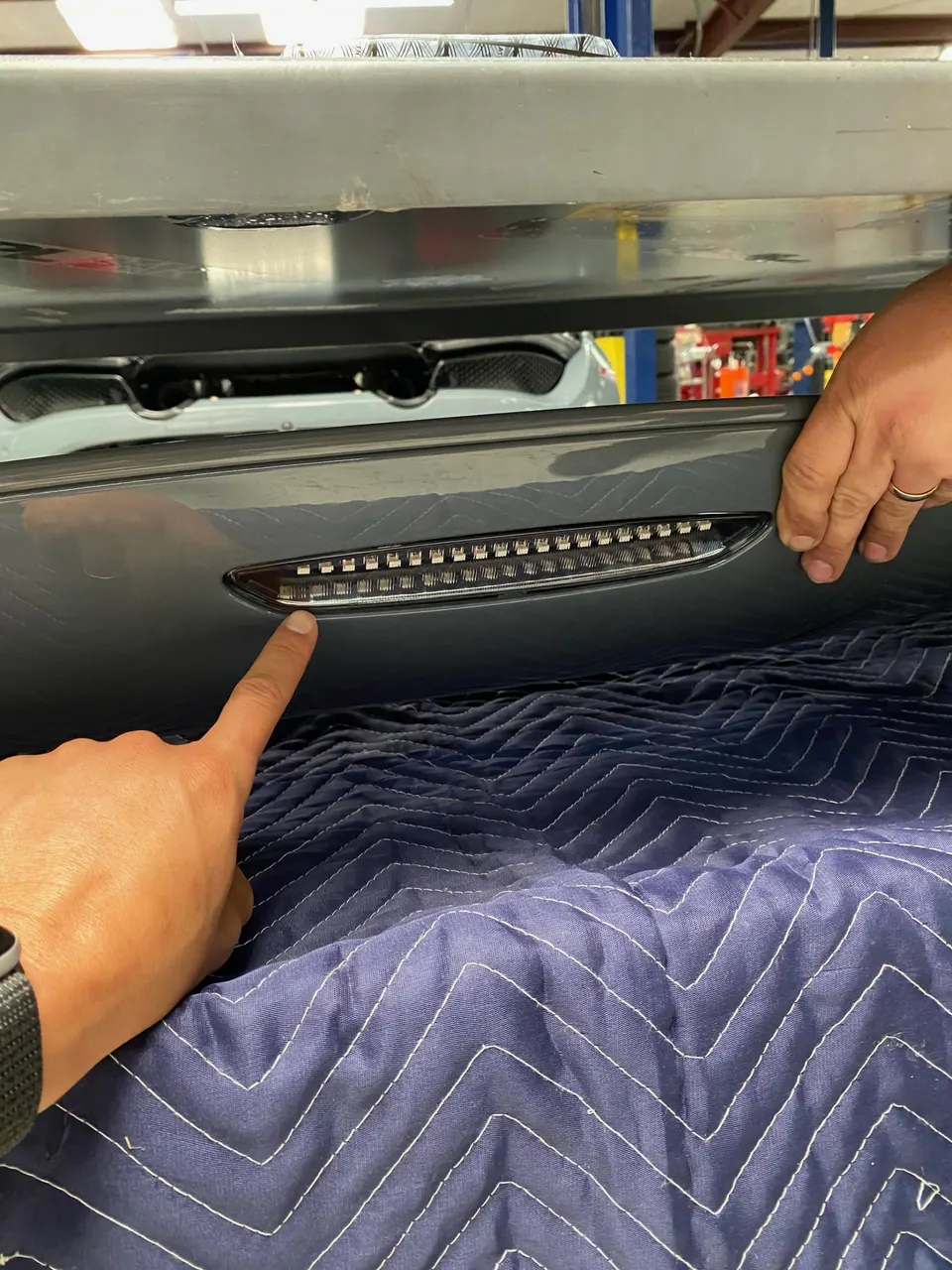 Hands installing an LED light strip into a car's exterior panel at an automotive performance shop.