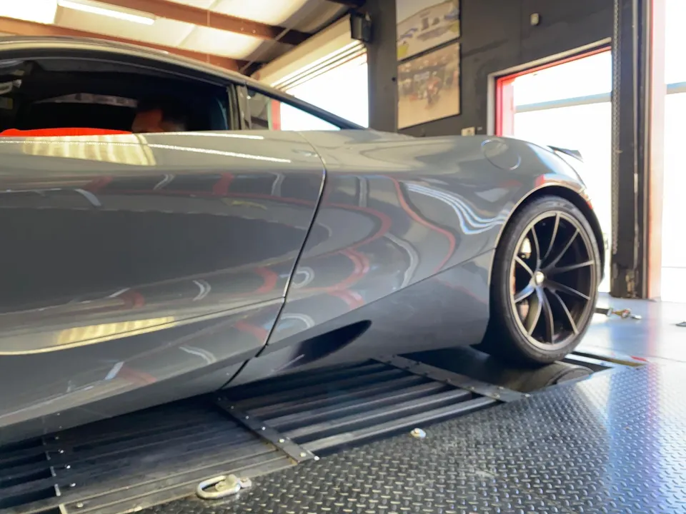 A grey McLaren supercar on a dynamometer at a performance tuning shop, undergoing testing.