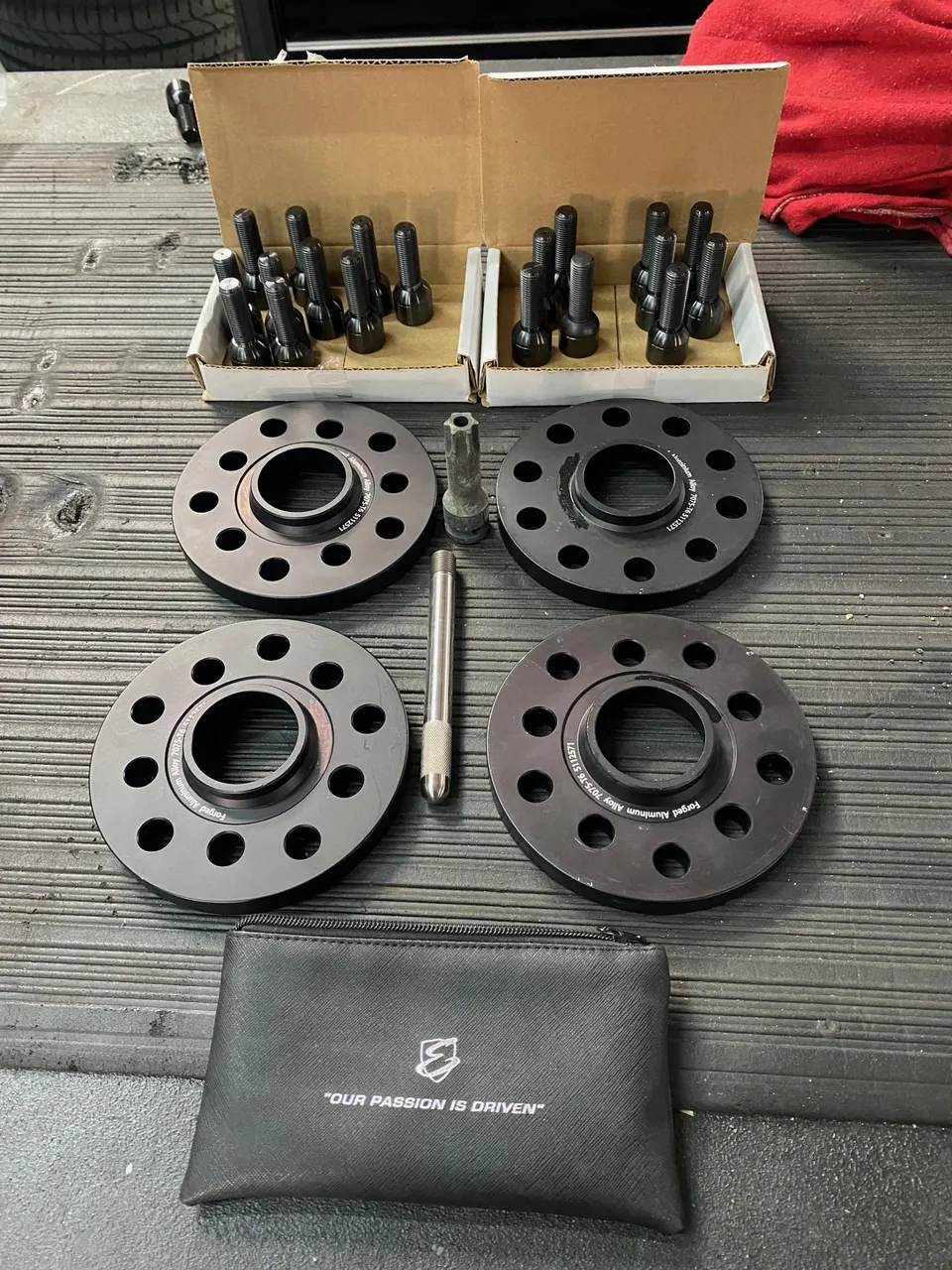 Black wheel spacers and lug bolts laid out on a workbench, ready for installation on a performance vehicle.