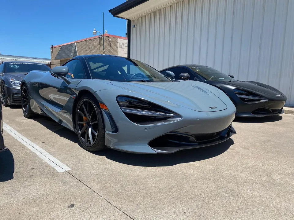 Two McLaren 720S supercars, one grey and one black, parked side by side in a lot on a sunny day.