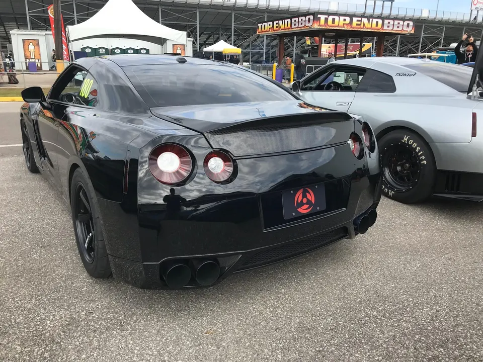 Two Nissan GT-Rs, one black and one silver with drag tires, parked at a drag strip event.