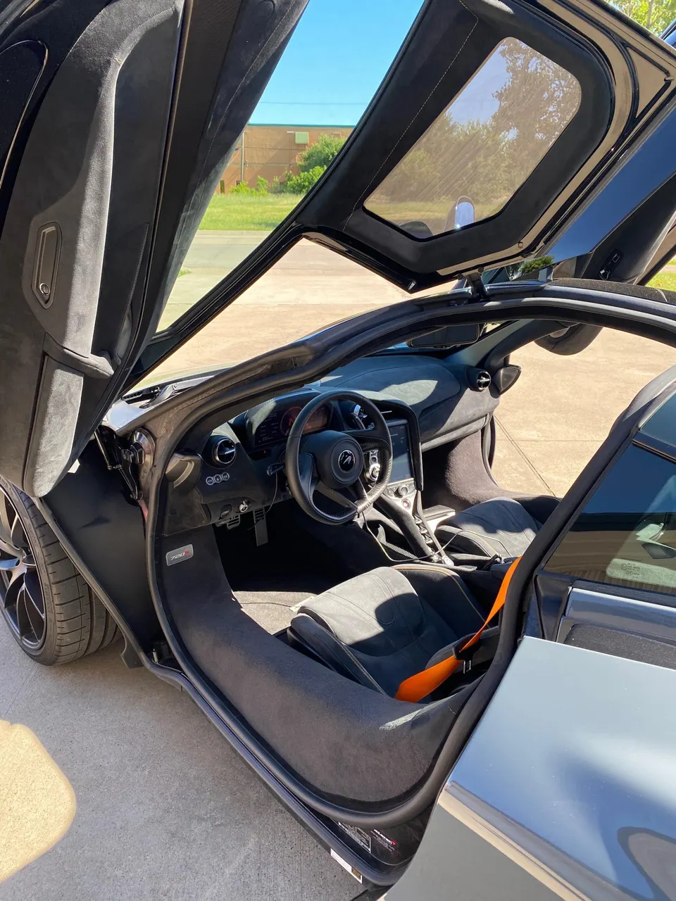 Detailed view of the black interior of a McLaren, featuring bucket seats with an orange harness, steering wheel, and open butterfly doors.
