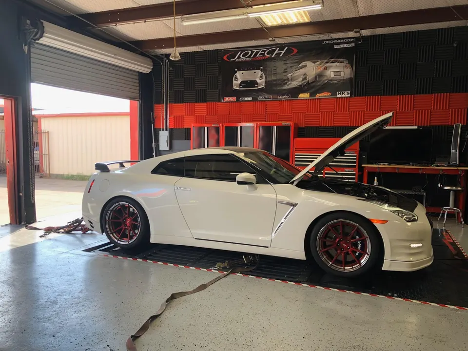 White Nissan GT-R on a dynamometer at Jotech Motorsports tuning shop with hood open, ready for tuning.