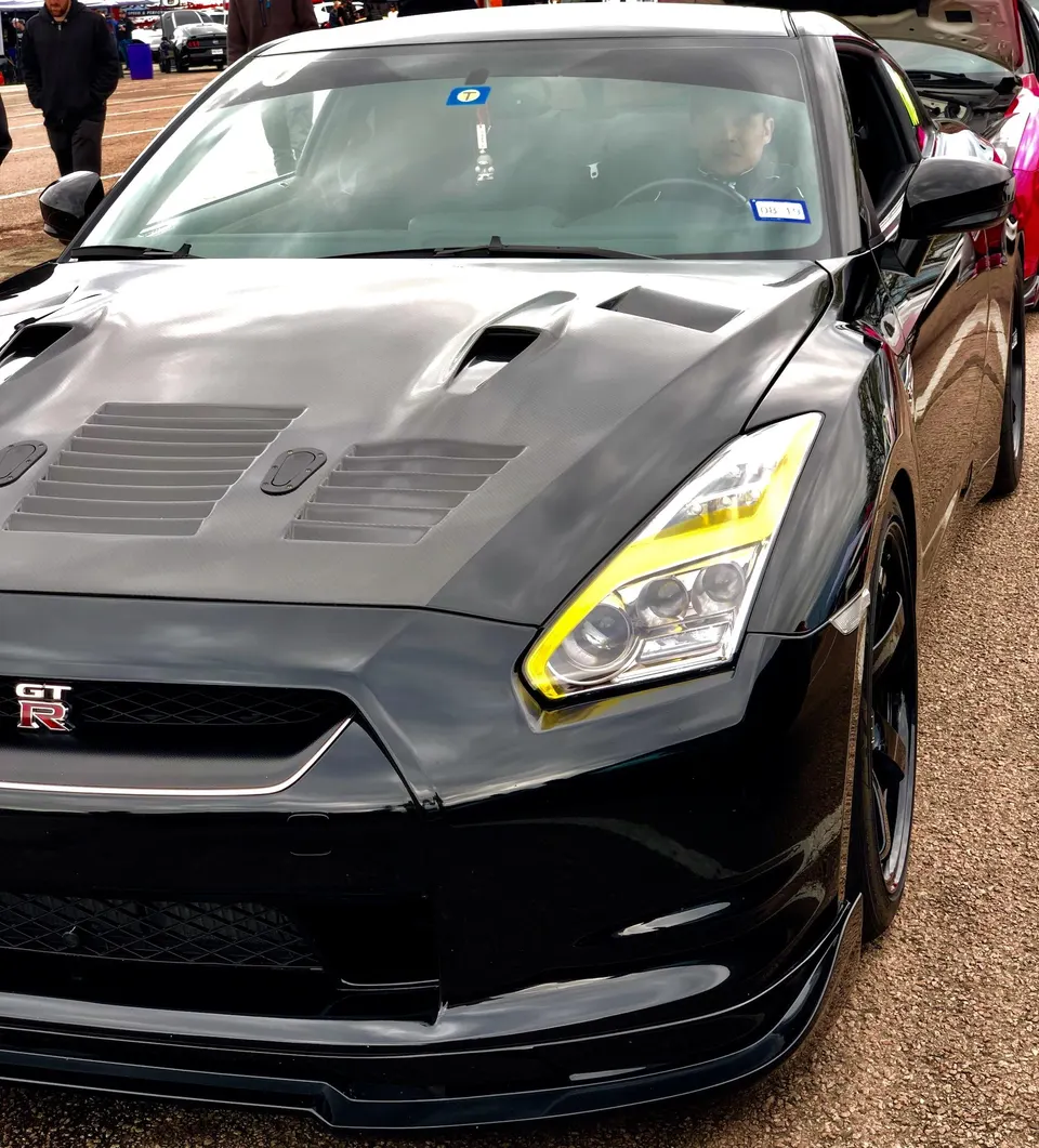 Black Nissan GT-R with a carbon fiber hood, yellow headlights, and front splitter parked outdoors.