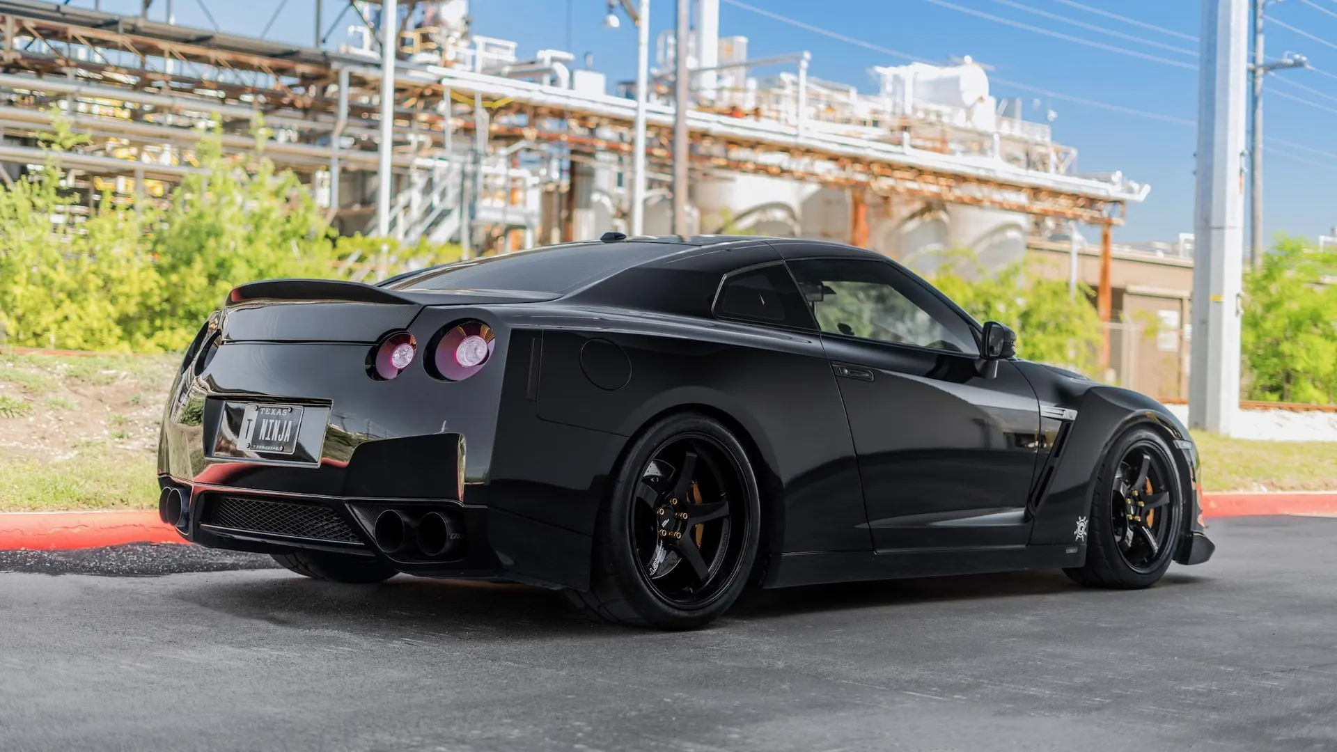 Black Nissan GT-R with aftermarket wheels and custom exhaust system parked in an industrial setting.