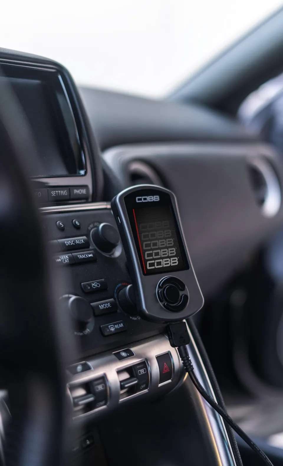 A Cobb Accessport tuning device mounted in the interior of a Nissan GT-R, displaying the Cobb logo.