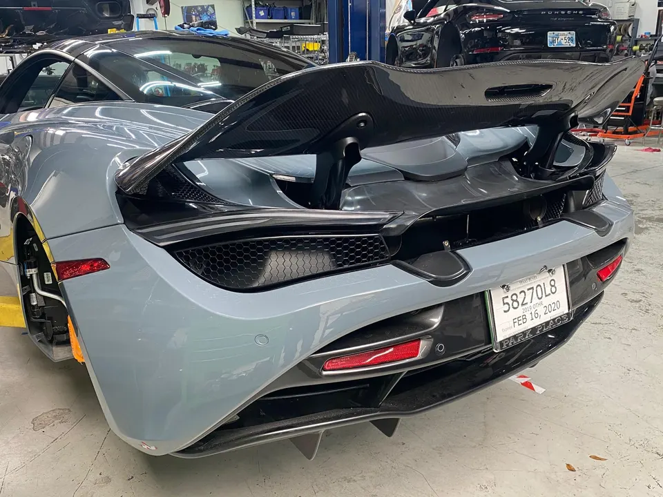 Rear view of a grey McLaren 720S in a shop, showcasing its carbon fiber active rear wing and diffuser.