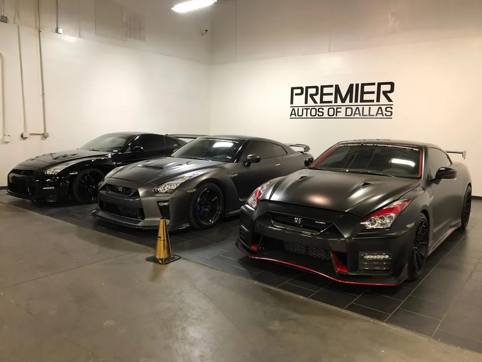 Three Nissan GT-R R35 sports cars, including black and matte grey models, displayed in the Premier Autos of Dallas showroom.
