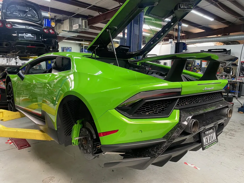 Bright green Lamborghini Huracan on a lift in a performance shop, with rear wheels removed exposing green brake calipers and carbon fiber diffuser.
