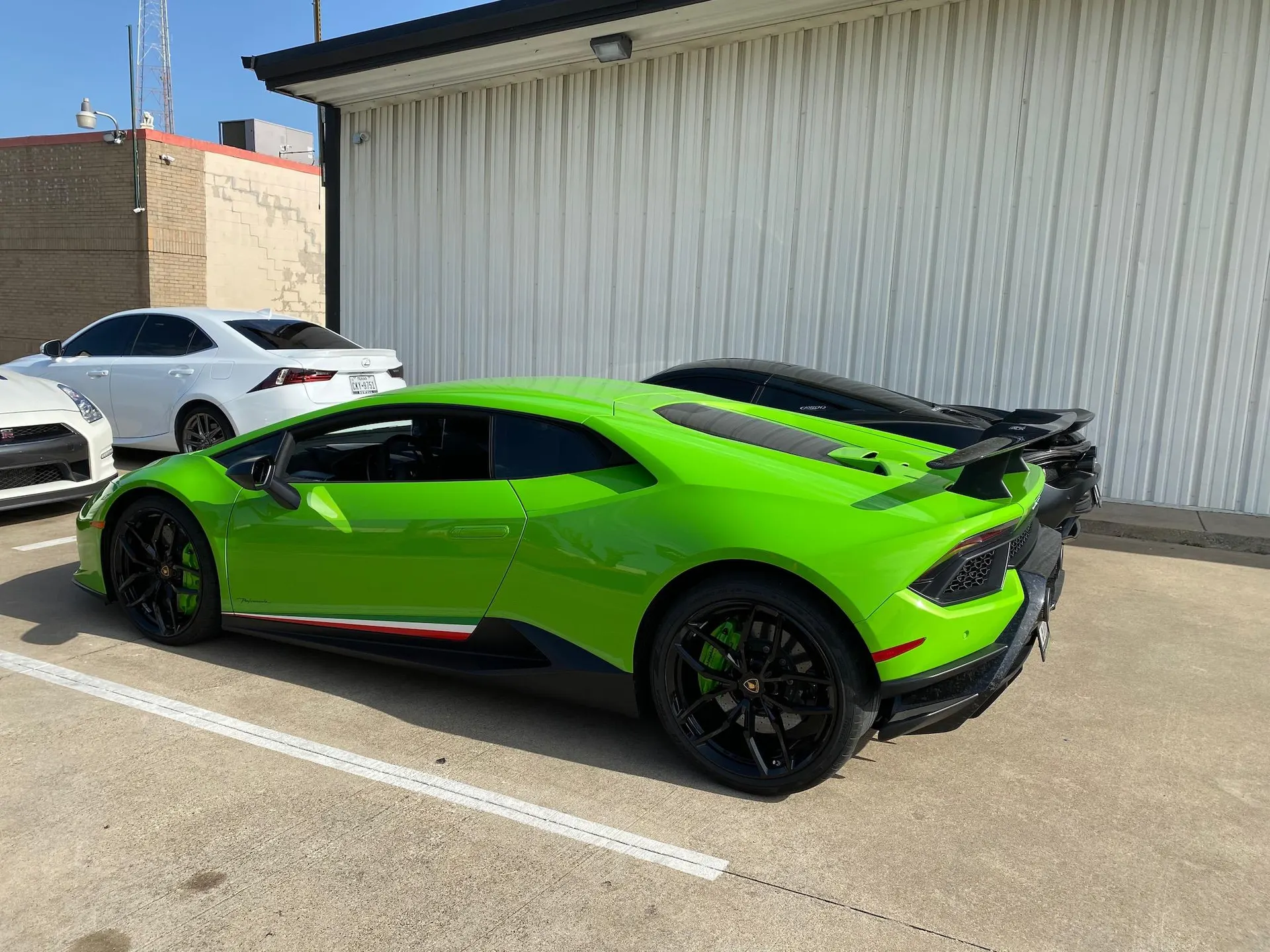Neon green Lamborghini Huracan parked next to a black McLaren, a white Lexus IS, and a Nissan GT-R outside a building.