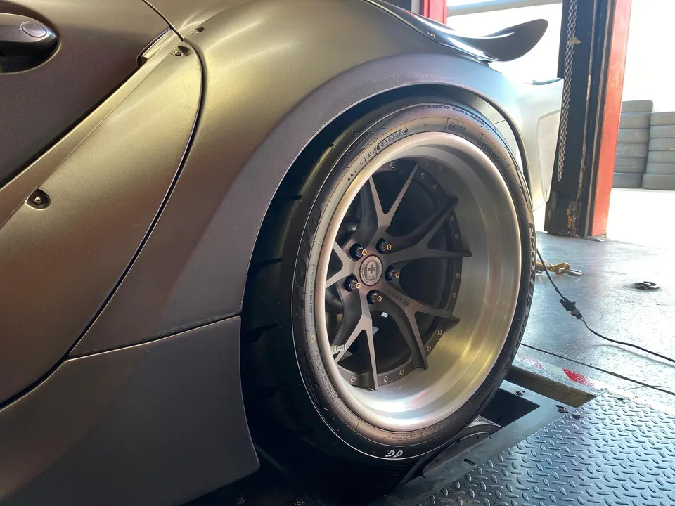 Close-up of a custom car's rear wheel on a dyno, showcasing HRE wheels and widebody fender.