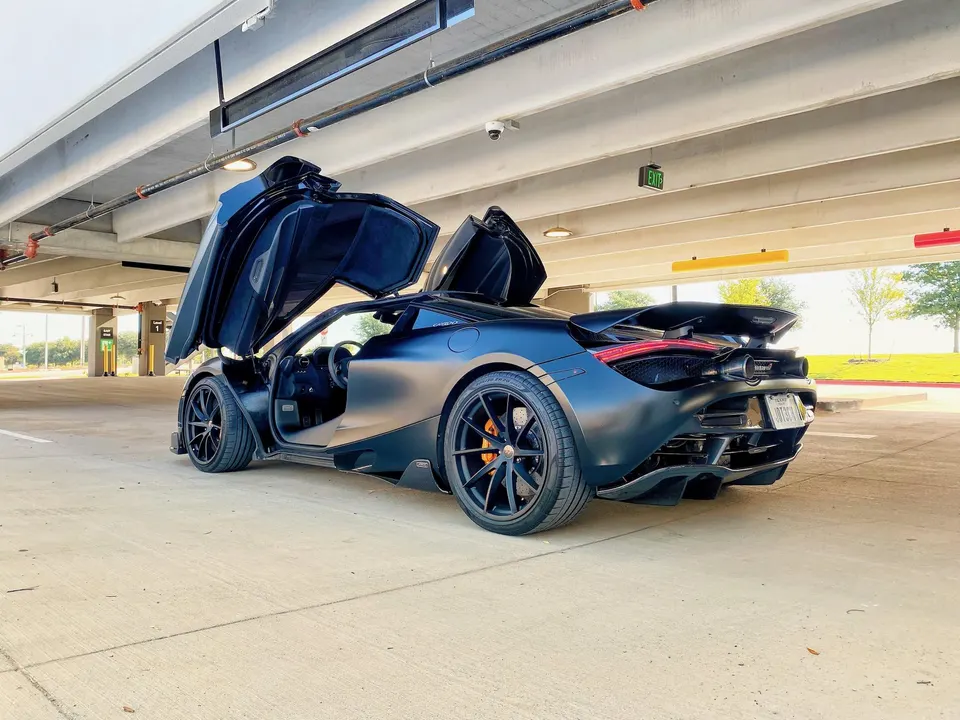 Matte black McLaren 720S with butterfly doors open, parked in a concrete parking structure.