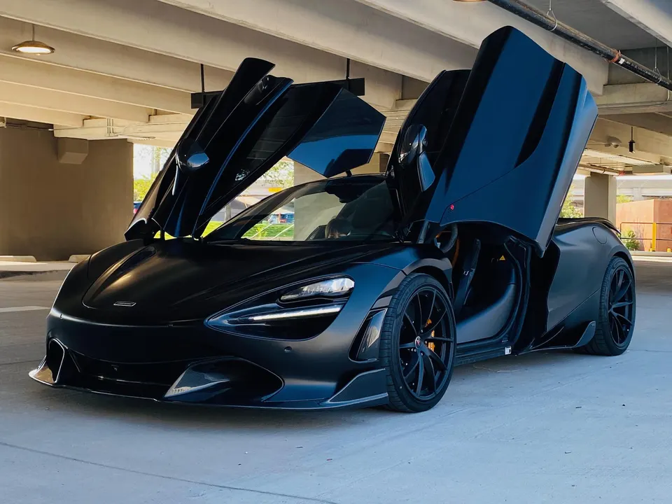 Matte black McLaren 720S supercar with butterfly doors open, parked in a clean concrete garage.