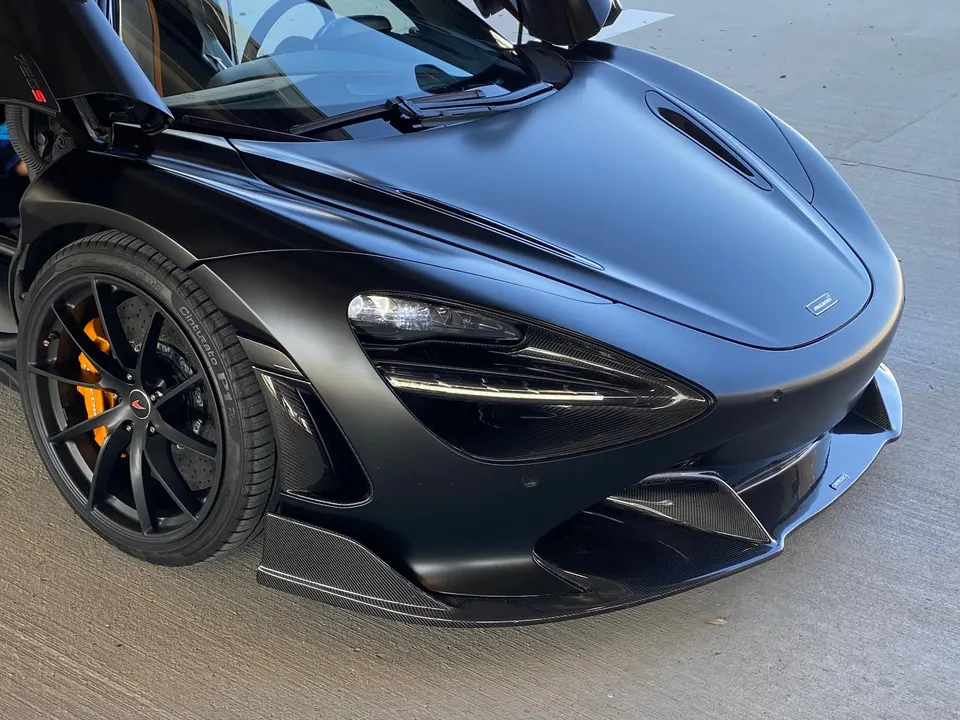 A matte black McLaren 720S with carbon fiber front splitter and orange brake calipers.