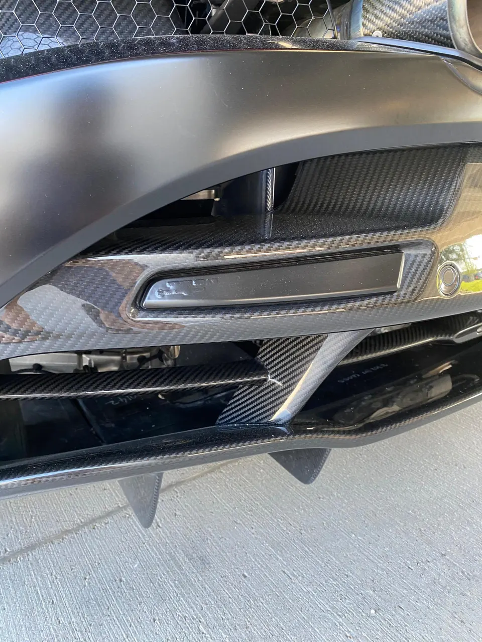 Close-up of a car's matte black front bumper with carbon fiber splitter and diffuser fins.