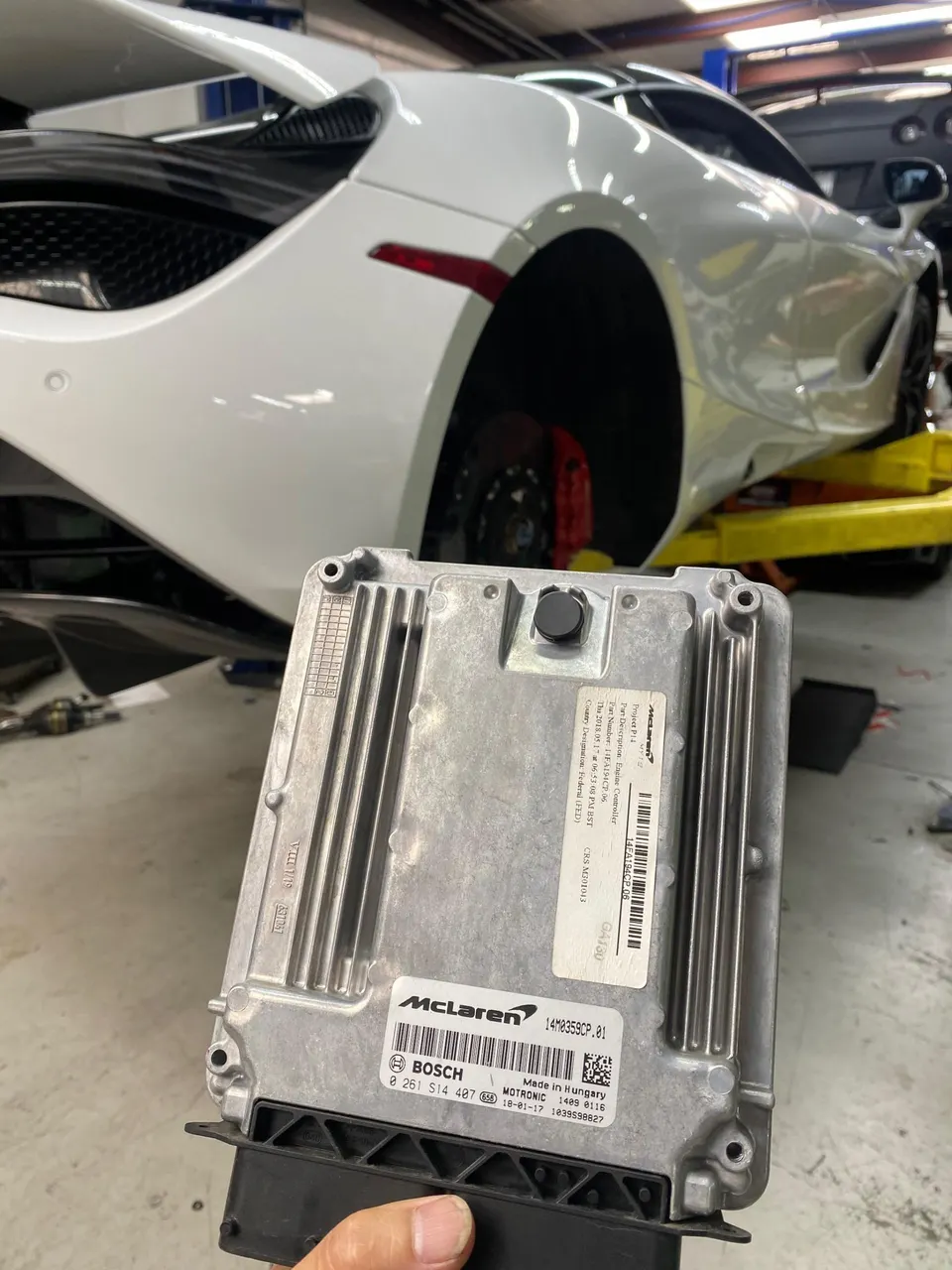 A McLaren supercar on a lift in a shop, with its Bosch Motronic ECU held in the foreground for tuning.