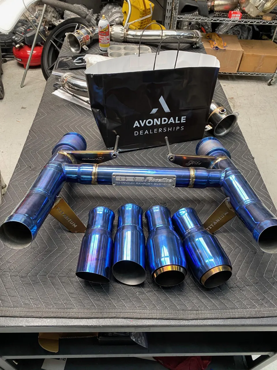 Blue titanium exhaust system with multiple tips laid out on a workbench in a performance shop.