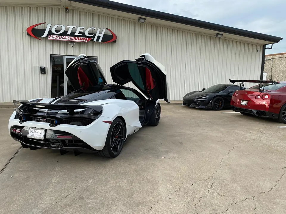 White McLaren 720S with doors open, black McLaren 720S, and red Nissan GT-R parked outside Jotech Motorsports.