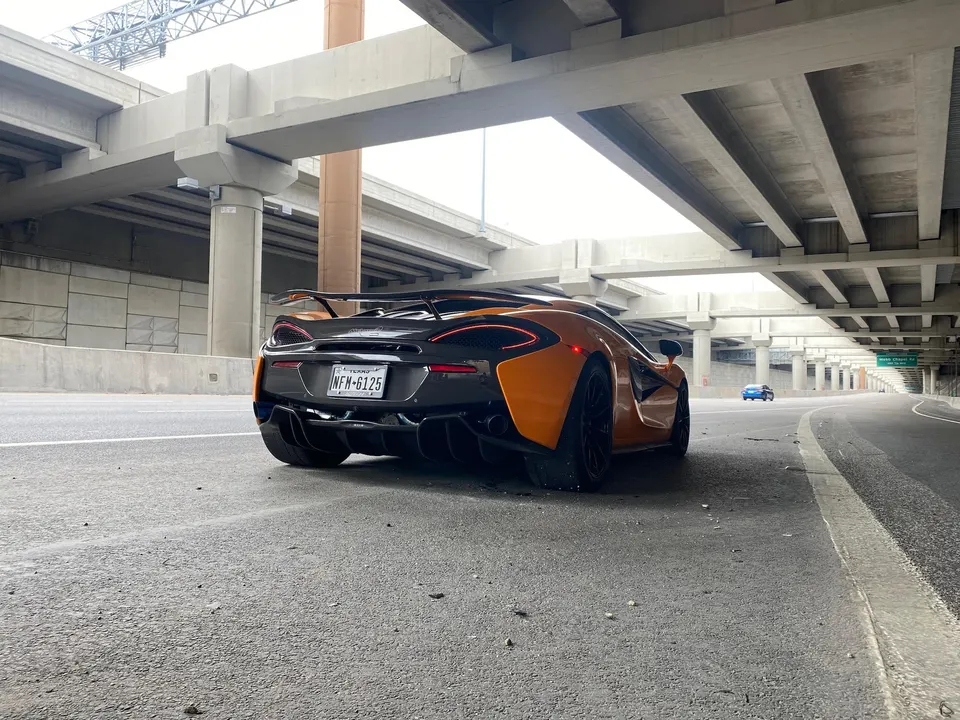 Orange McLaren 570S parked on a highway ramp under an overpass, showcasing its rear diffuser and wing.