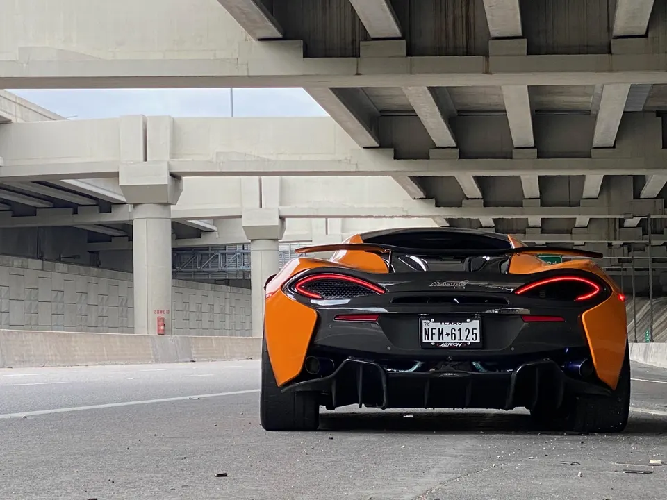 Orange McLaren supercar parked under a concrete overpass, showcasing its rear design and exhaust.
