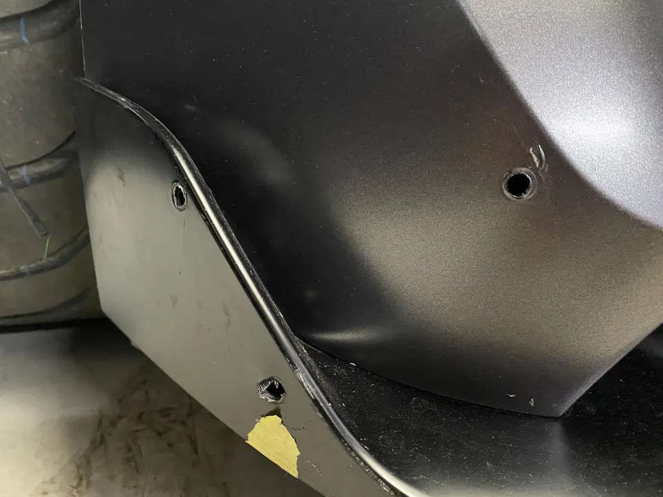 Close-up of a black aftermarket rear diffuser or aero piece being installed on a car, showing mounting holes.