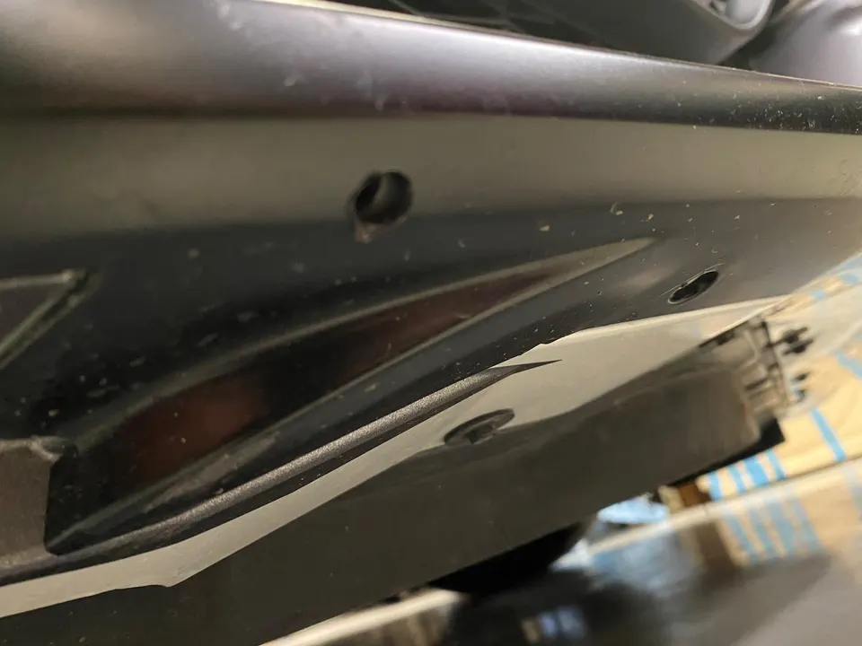 Close-up detail of a car's black plastic underbody panel with a visible fastener and a small hole, possibly for drainage or mounting.