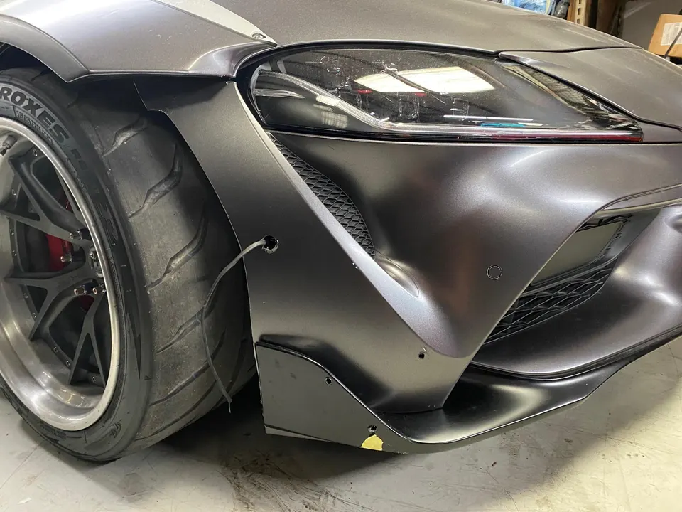 Close-up of a matte gray Toyota Supra with a widebody kit, front splitter, and performance wheels.