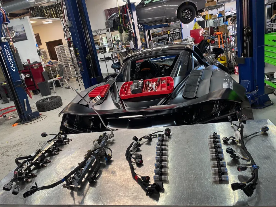 McLaren supercar in a performance shop with fuel injectors, fuel rails, and wiring harnesses laid out on a workbench.