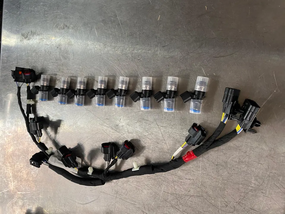 Aftermarket fuel injectors and a custom wiring harness laid out on a metal workbench for a performance build.