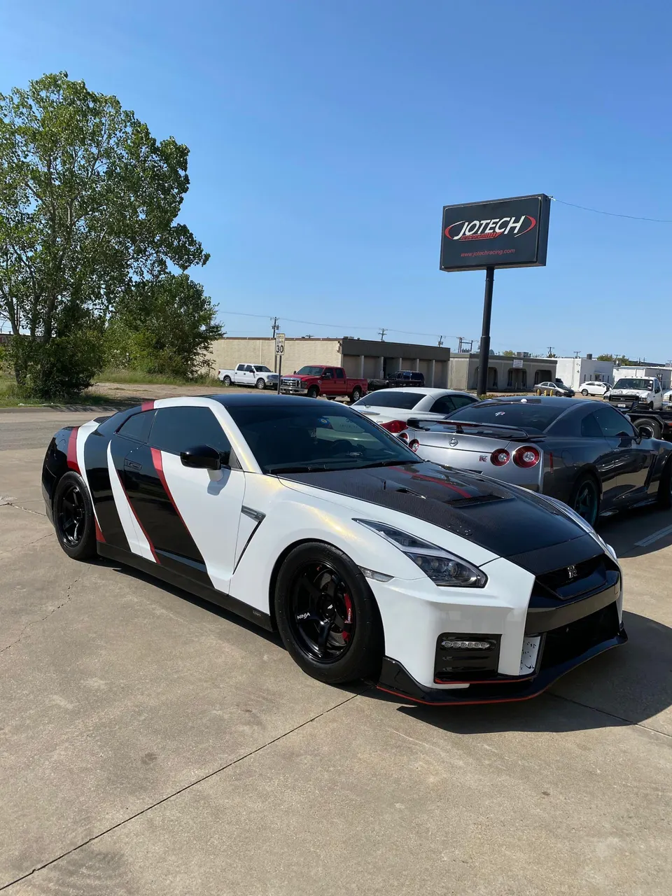 White, black, and red custom-wrapped Nissan GT-R R35 with aftermarket wheels parked outside Jotech Motorsports.