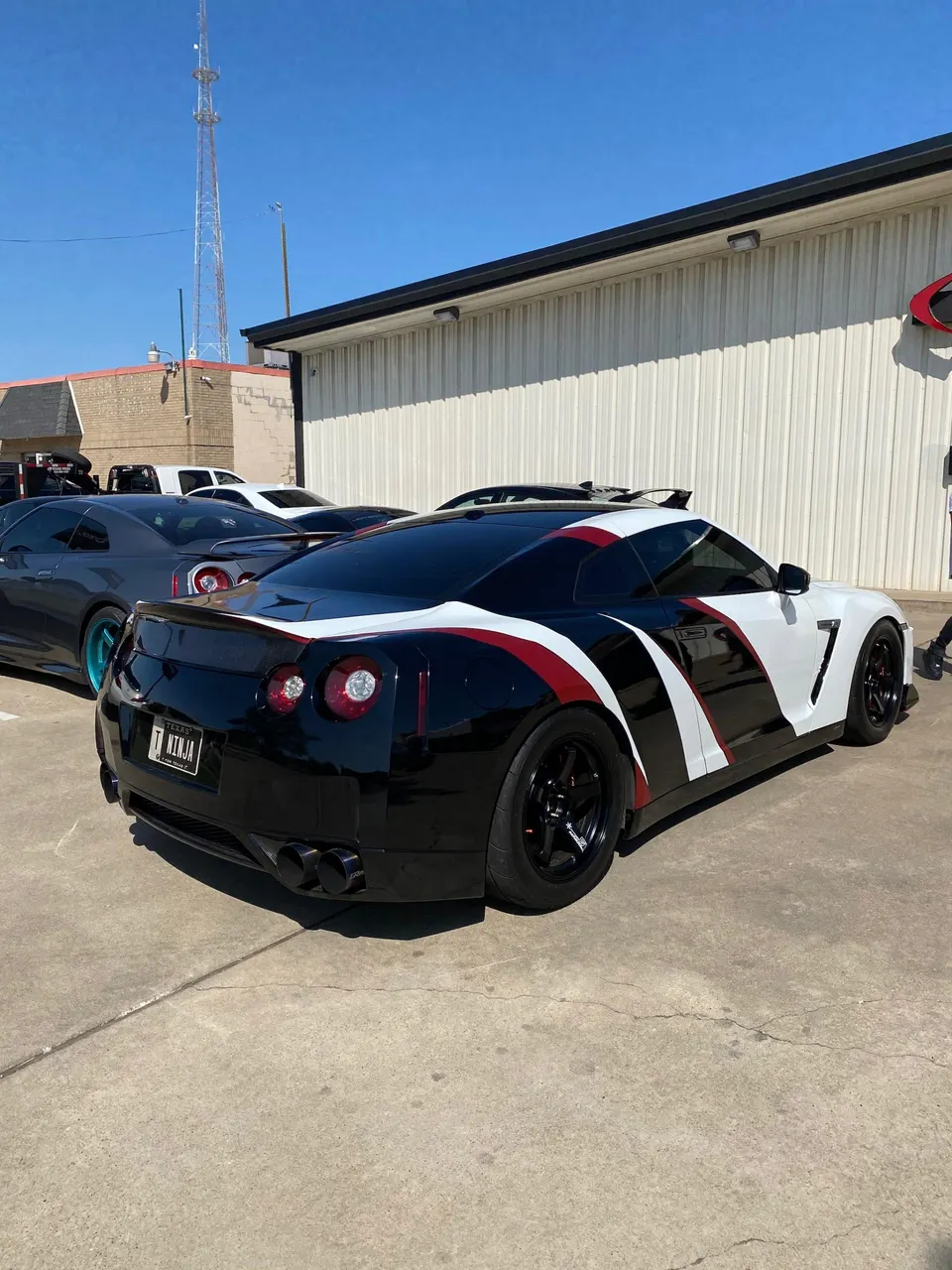 Custom black and white Nissan GT-R with red accents and aftermarket wheels parked outside a performance shop.