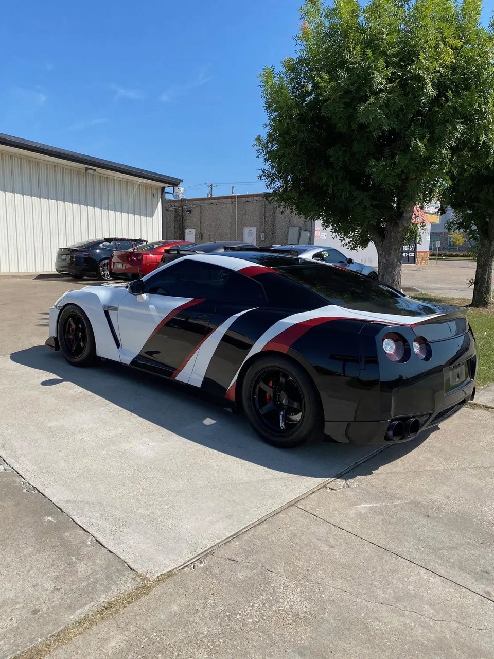 A Nissan GT-R with a custom white, black, and red livery parked outdoors on a sunny day.