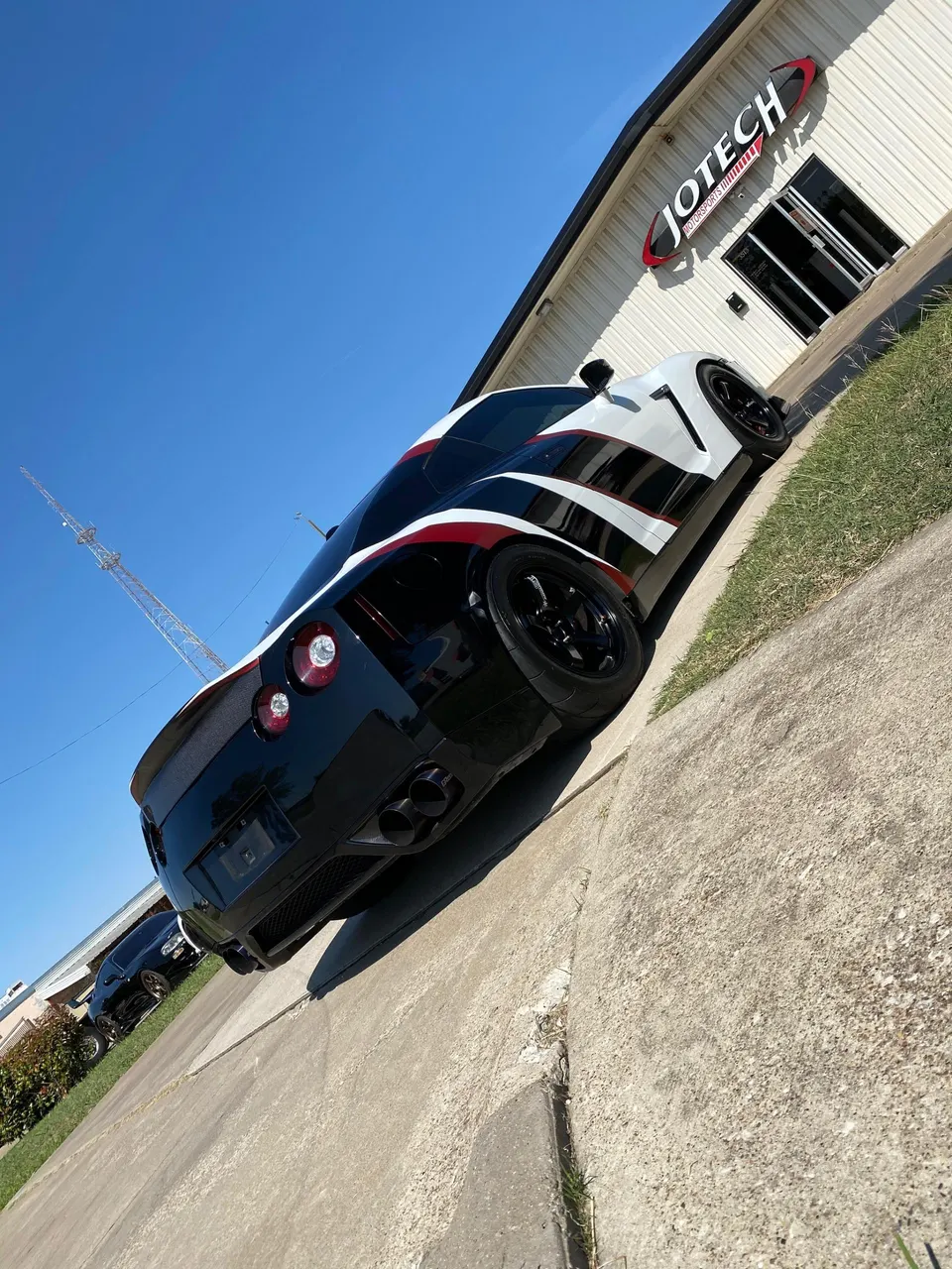 A black and white Nissan GT-R with red accents parked outside Jotech Motorsports, showcasing its custom exterior and aftermarket exhaust.