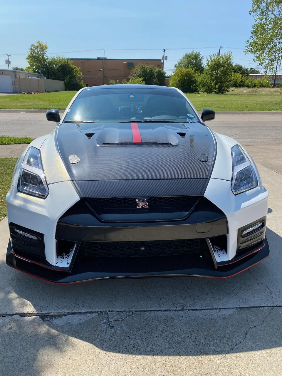 Front view of a white Nissan GT-R R35 with a carbon fiber hood, red stripe, and custom front splitter.