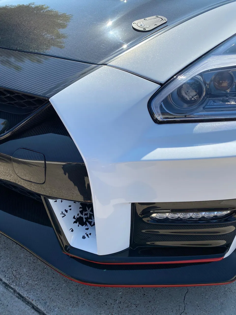 Close-up of a white Nissan GT-R's front end, showcasing its carbon fiber hood, hood pins, and front splitter.