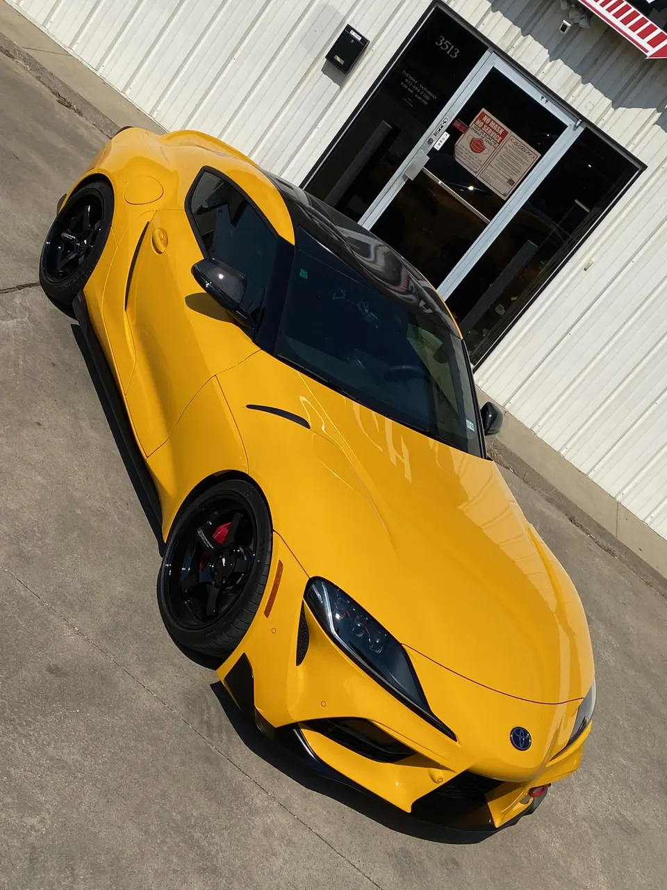 Yellow Toyota Supra A90 parked outside a building, showcasing its sleek design and aftermarket wheels and red brake calipers.