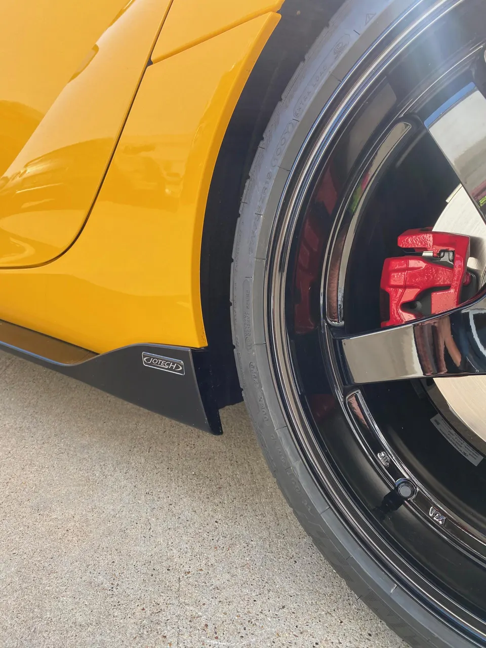 Close-up of a yellow car's black wheel, red brake caliper, and Jotech side skirt.