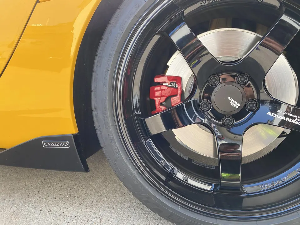 Close-up of a yellow car's black Advan wheels with red brake calipers and Jotech side skirt.