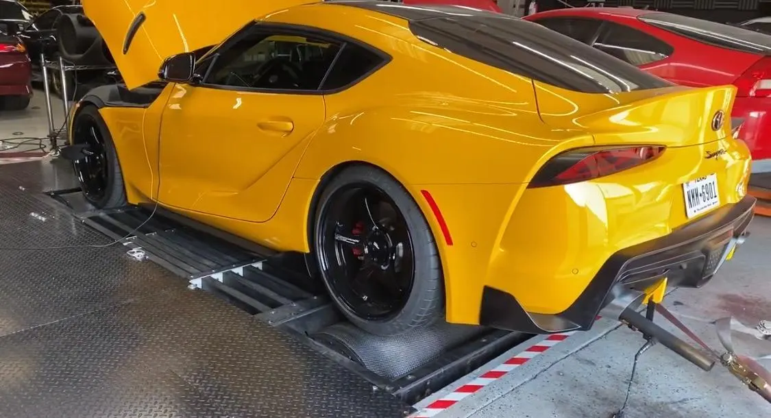 Yellow Toyota Supra on a dynamometer for performance testing with aftermarket wheels.