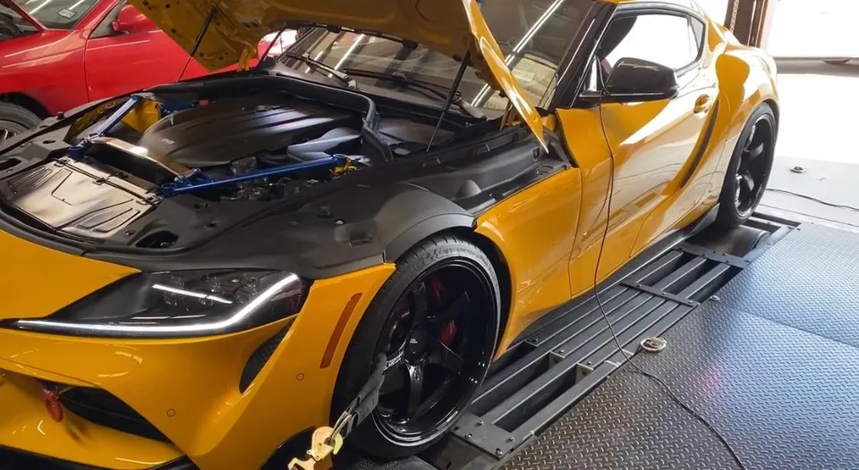 Yellow Toyota Supra on a dynamometer with the hood open, ready for performance testing.