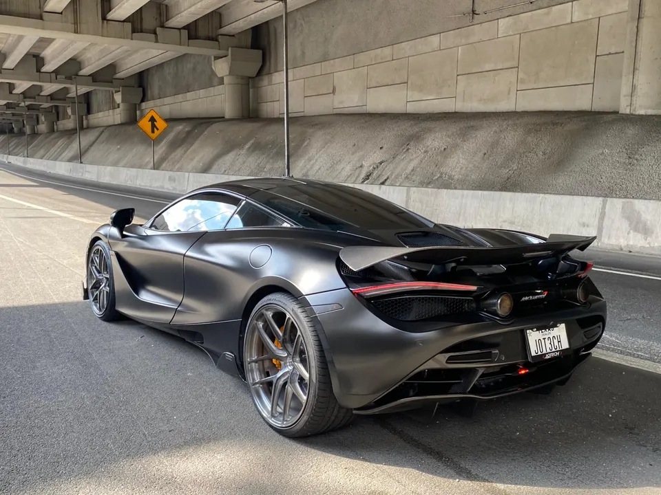 Matte black McLaren 720S supercar with custom wheels and an active rear wing parked under an overpass.