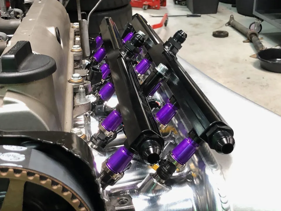 Close-up of aftermarket black fuel rails and purple fuel injectors installed on a performance engine.