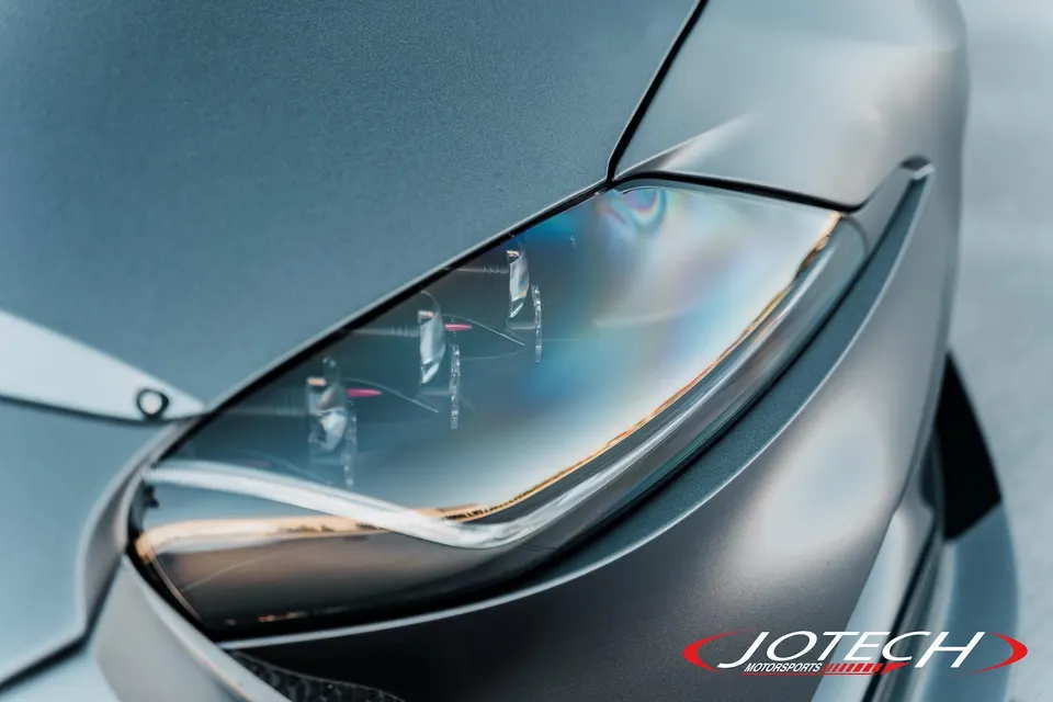 A close-up detail of a modern car's sleek headlight and matte grey front fender.