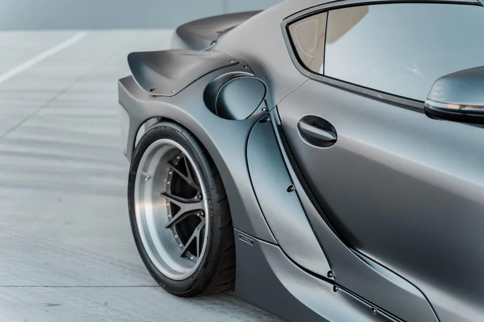 Close-up of a grey Toyota Supra with a widebody kit, aftermarket wheels, and a rear spoiler.