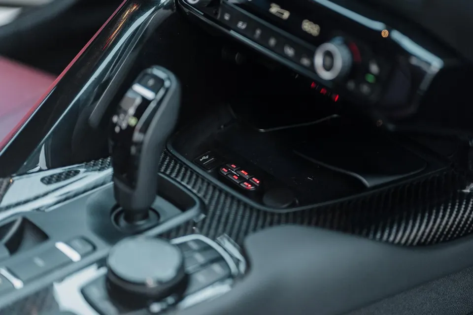 Close-up of a car's interior, featuring a carbon fiber center console, automatic shifter, and electronic controls.